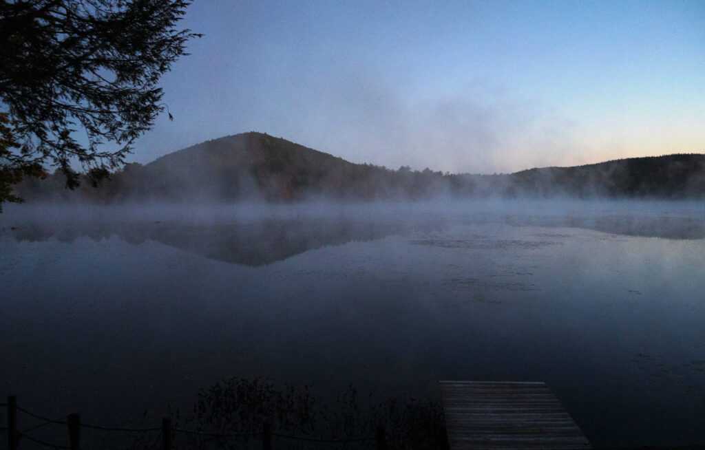Fog over a lake, surrounded by trees during autumn sunrise.