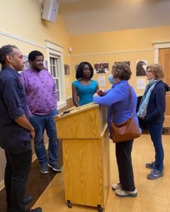 Three writers stand behind a podium, talking to two other writers who came to the reading.