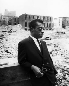 James Baldwin stands among the ruins of buildings in Harlem.